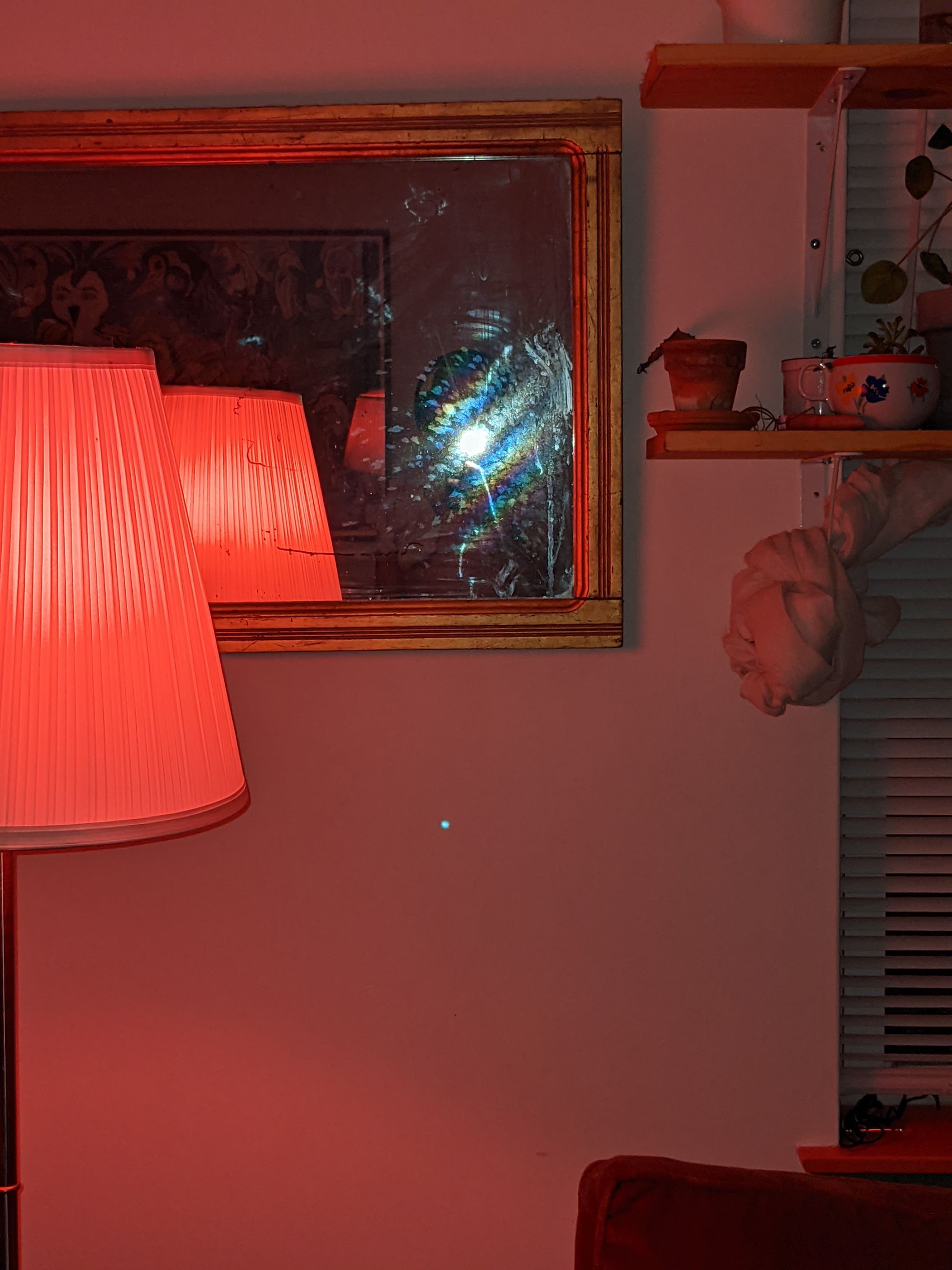 in a mirror on a living room wall, a flash obscures a man taking his own photograph. pink light from a visible lamp dominates the space.